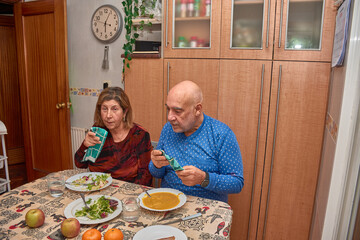 An elderly couple shares a home-cooked meal in their dining room with affectionate gestures and a sense of connection that reflect lasting love.