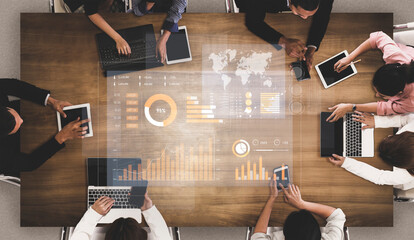A diverse group of professionals collaborates around a wooden table, using laptops and tablets to analyze digital data visualizations with charts and maps. Scalp