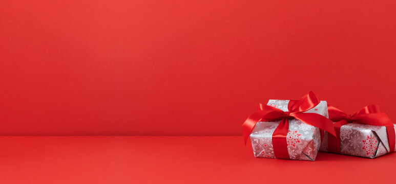 Christmas gifts on a red table. Two elegantly wrapped silver gift boxes with bright red snowflakes on a red background. Perfect for holiday promotions, advertising banners, or Christmas cards.