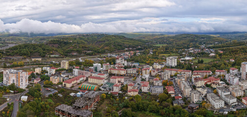 Fototapeta premium Panoramic drone view of Rrëshen with residential blocks, rolling hills and low clouds drifting over the autumn landscape.