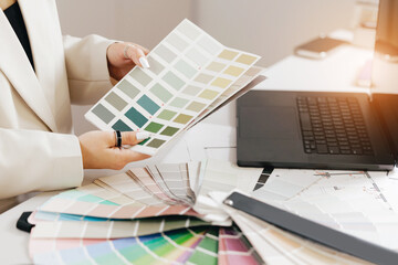 Female designer choosing color swatches in modern office for creative project with notebook