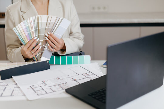 Female designer reviewing color swatches and floor plans in modern office, online video call with client on computer