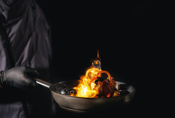 Male chef flambe cooking with fire in dark kitchen
