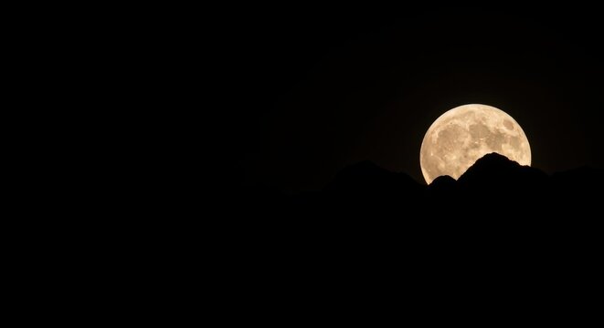 Full moon rising over dark mountain silhouette