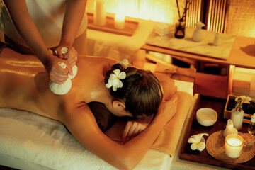 Hot herbal ball spa massage body treatment, masseur gently compresses herb bag on woman body....