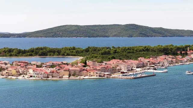 Breathtaking aerial view of a charming small Krapanj island town featuring traditional stone houses with red roofs, a busy marina filled with boats, and a lush green forest
