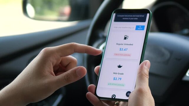 Closeup of a mans hands in a parked car analyzing current fuel prices for different types of gasoline on a smartphone. This clip captures a practical moment of financial planning for vehicle owners.