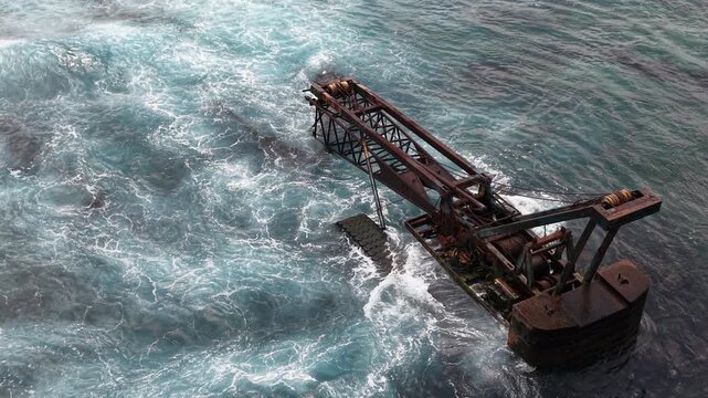 Escavator wreck sea coast with waves of Bali, Nusa Lembongan Island drone aerial shot in Indonesia surrounded by beautiful jungle and tropical blue sea water and cliffs