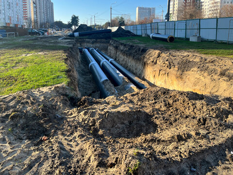 Large trench with newly installed insulated steel pipes for district heating or water supply in city residential area, concept of urban infrastructure, utility repair and civil engineering works.