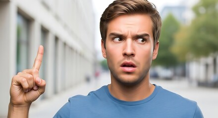 A man with a surprised expression pointing his finger up in an outdoor urban setting with blurred background