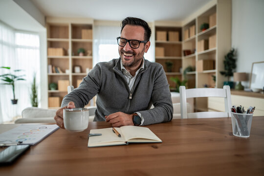 Smiling man enjoying coffee at home office working remotely