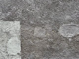 Close-up of a rough gray concrete wall with irregular patches and textured surface, showing signs of repair and unfinished construction detail.