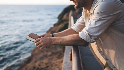 Man holding a notebook leaning on a railing by the ocean