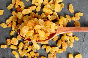 Yellow raisins lie on a wooden spoon on a black background.	