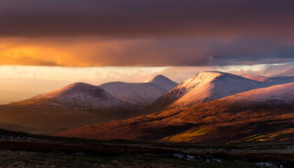Snow Capped Peaks Of The Cairngorms Under A Golden Sunrise With Dramatic Skies And Rolling Hills