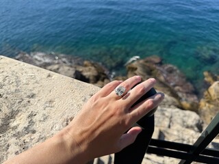 Female hand with diamond engagement ring by the sea in Croatia, showing romance and vibrant color.