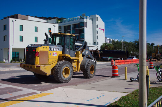 Yellow Deere Wheel Loader At Urban Construction Site With Barriers And Modern Buildings. Editorial Use Only, Nov 11, 2025. St. Petersburg, FL USA. Sits on a city street, surrounded by orange cones, ba