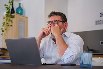 Tired mature man rubbing eyes from working on laptop