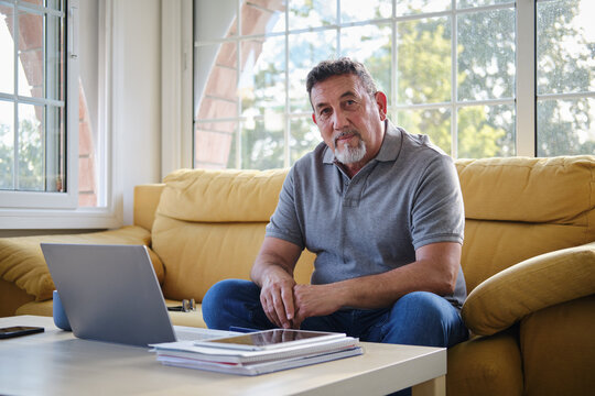 Mature caucasian man studying remotely from home on couch looking at camera