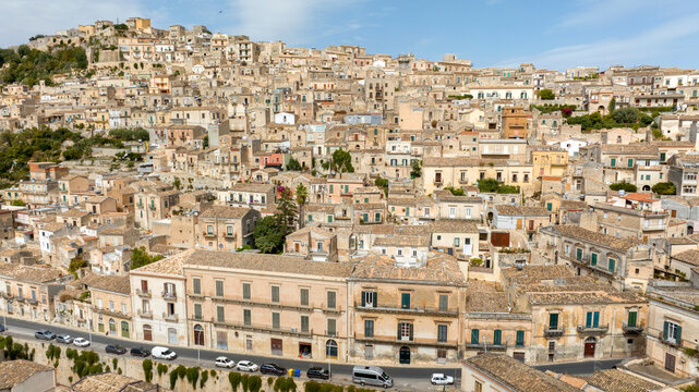 Aerial view of the historic center of Modica, in the province of Ragusa, Sicily, Italy. Many small houses and buildings perched on a hill. - Powered by Adobe