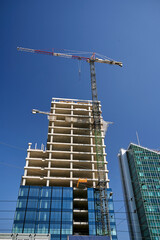 A crane at the construction site of an office building and a fragment of a modern glass and steel building in Poznan