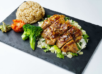 Teriyaki chicken meal served with brown rice, vibrant broccoli, crisp greens, and spicy kimchi for a delightful experience.