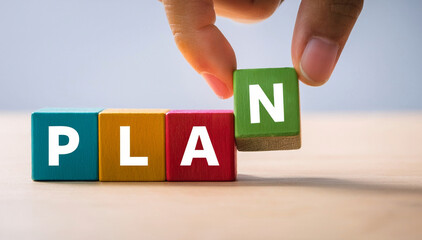 Colorful wooden blocks forming the word PLAN with a hand placing the final letter, symbolizing strategy, goal setting, business planning, decision making, and organization in a creative concept.