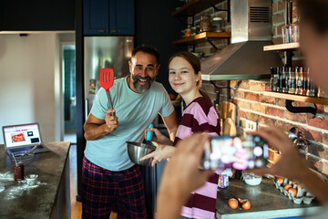 Smiling adult father and teen daughter baking in home kitchen