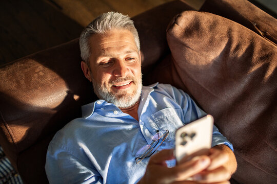 Mature man smiling while using smartphone on couch at home