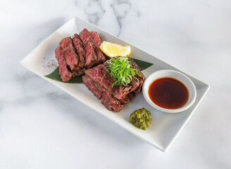 Seared steak tataki. A culinary masterpiece with fresh green onions and zesty lemon, plated for delight.