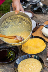 Man Preparing Rustic Polenta with Sheep Cheese on Open Fire. Authentic Countryside Cooking. Rustic Outdoor Meal. Traditional Village Cuisine. Heritage Food Scene
