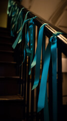 Turquoise ribbons hanging along a dark wooden staircase railing with soft warm lighting creating a festive decorative atmosphere, concept of holiday decor and seasonal celebration