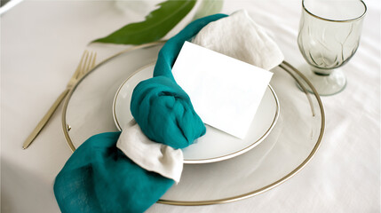 Top view of elegant table setting with teal linen napkin, white plate and blank card on soft neutral tablecloth creating modern wedding styling, concept of table decor and event stationery