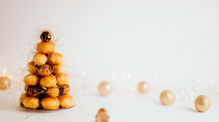Golden croquembouche tower decorated with delicate sugar threads and festive lights on a bright white background