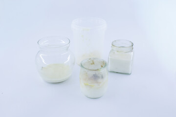 A set of small glass and plastic containers shows spoiled dairy with visible mold growth, captured on a clean white background for food safety and waste documentation.
