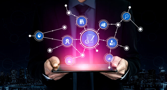 A businessman stands in a futuristic city at night, holding a tablet displaying vibrant digital marketing icons and connections. Ideal for business and technology themes. Tessel