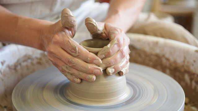 Hands shaping clay on pottery wheel, traditional ceramic craftsmanship, artist molding wet clay into pot, artisan creating handmade earthenware in workshop, creative pottery making process  