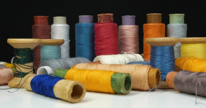 Beautiful multi-colored spools of thread lie on white table and rotates on black background