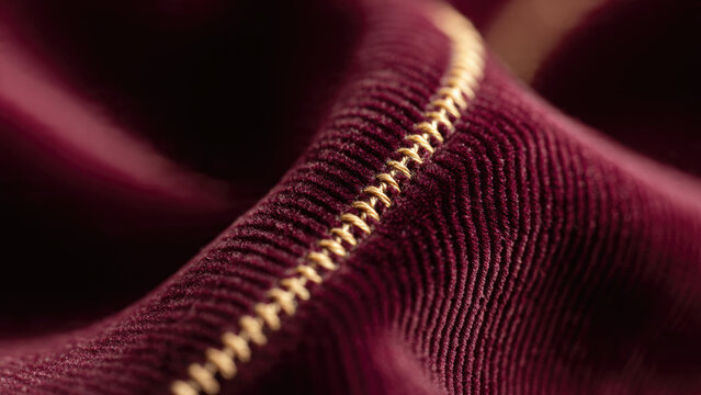 Macro shot of rich burgundy corduroy fabric with intricate gold stitching, highlighting its textured surface and elegant craftsmanship.