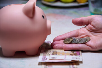 A hand is putting coins into a pink piggy bank