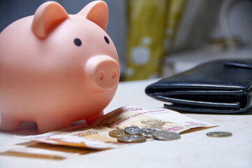 A piggy bank sits on a table with a wallet and some coins
