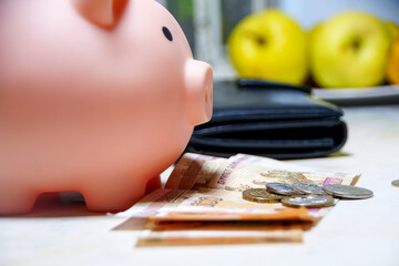 A pink piggy bank sits on a table with a pile of money and coins