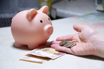A hand is holding a piggy bank and coins