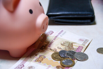A piggy bank is sitting on a table with a stack of Russian banknotes and coins