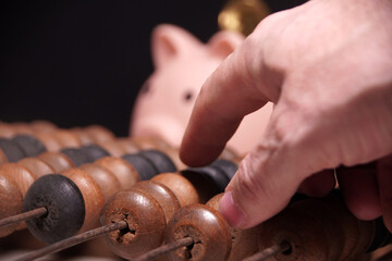 A hand is pointing at a piggy bank on a wooden abacus