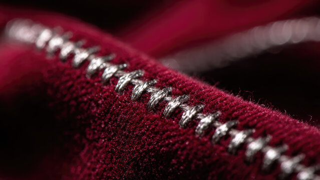 A detailed macro shot showcasing exquisite silver metallic stitching on rich, textured crimson red fabric, emphasizing craftsmanship and luxurious textile detail.