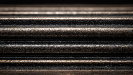 A detailed close-up of textured, dark bronze or aged metallic horizontal ridges and grooves, creating an abstract, industrial pattern of light and shadow.