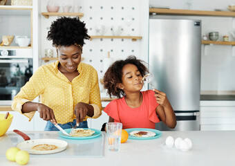 Portrait of mother, father and daughter preparing and eating pancakes in the kitchen at home