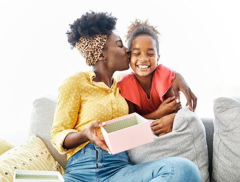 Portrait of a girl child daughter covering mother's eyes and giving her present for her burthday or mother's day at home