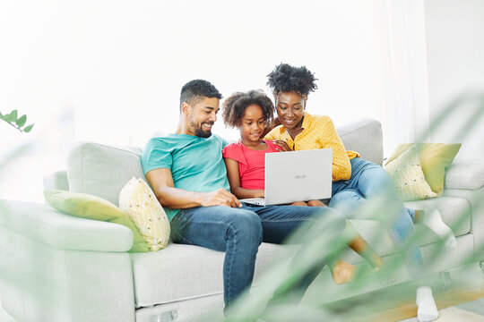Mother, father and daughter doing homework with laptop at home. Mom, dad and teenage black girl happy using laptop. Teen girl and parents sitting at home working with notebook